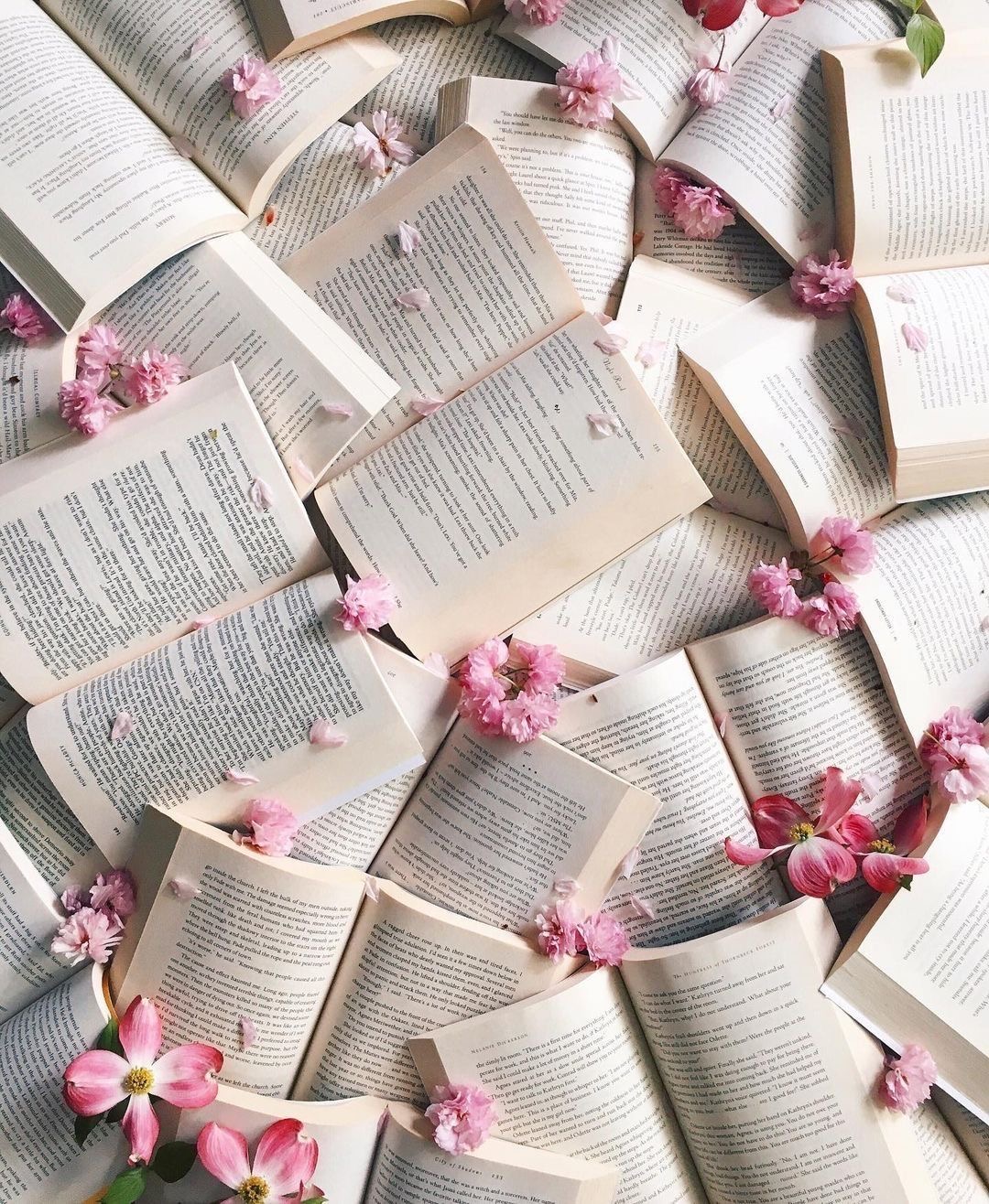A tabletop scattered with open books and pink cherry blossoms